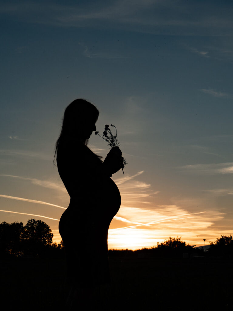 Silhouette einer schwangeren Frau in der Abendsonne bei einem Outdoor Babybauchshooting im Freien