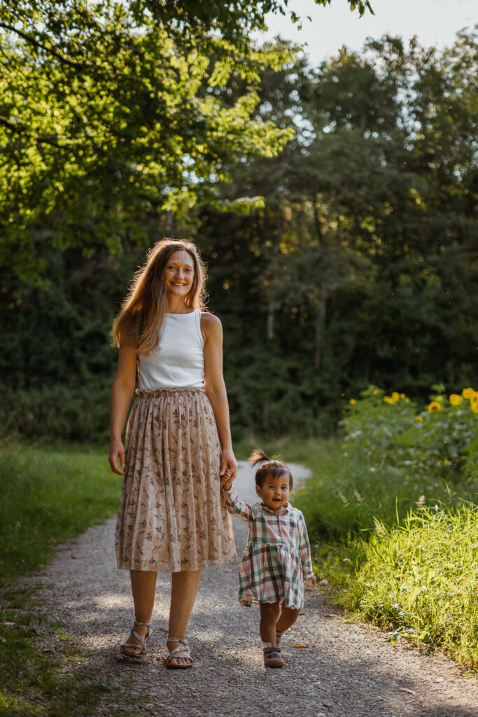 Mutter geht mit ihrer kleinen Tochter an der Hand bei einem Outdoorshooting im sanften Abendlicht in Marktheidenfeld spazieren