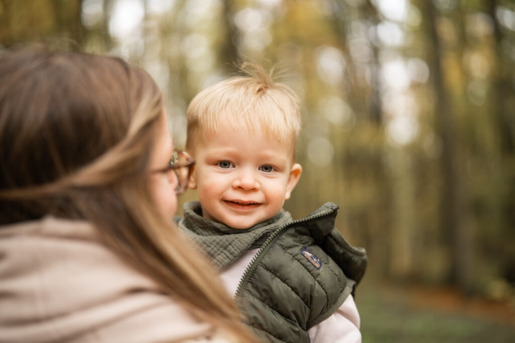 Kleines Kind auf dem Arm der Mutter, lächelt in die Kamera während eines Familienfotoshootings von Mirjam Scherg in Marktheidenfeld