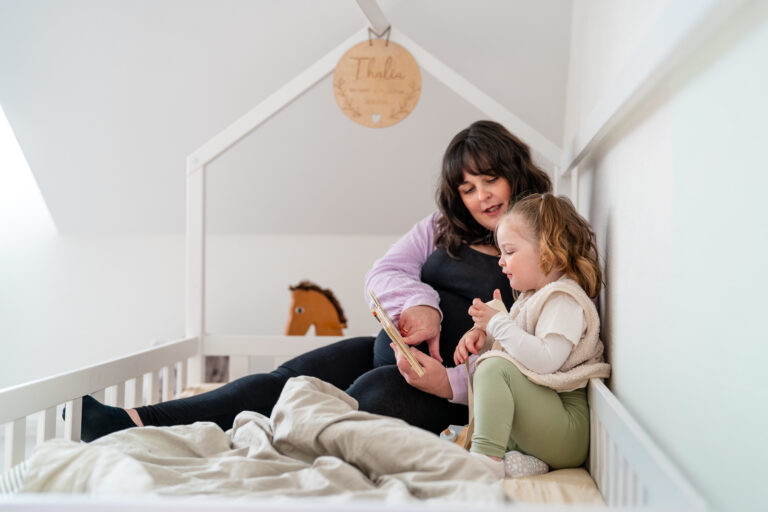 Mama liest mit Kind auf dem Bett ein Buch bei einer Homestory