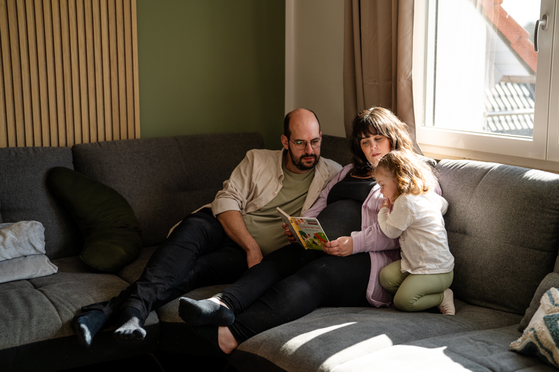 Eltern mit Babybauch und Kleinkind sitzen auf Couch im Wohnzimmer