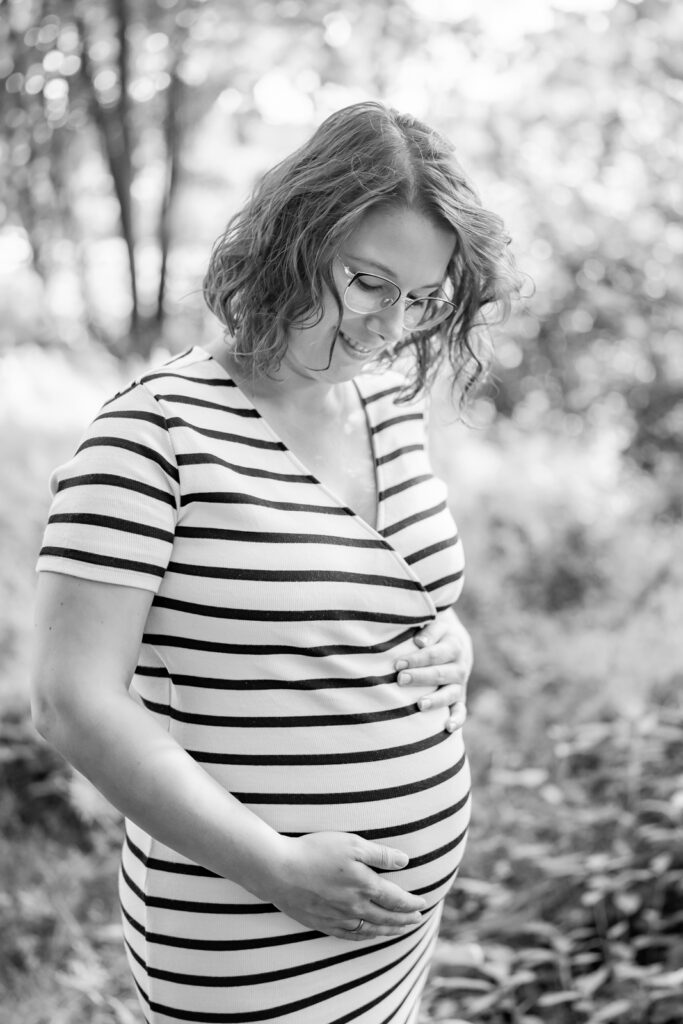 Babybauchfotos draußen im Grünen mit werdender Mutter die ihren Bauch hält