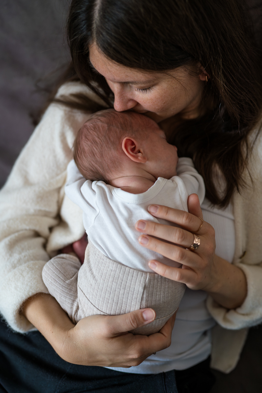 Eine Mutter hält ihr Neugeborenes Baby ganz dicht und küsst es auf die Stirn